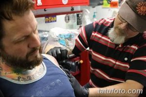 Фотография процесса нанесения татуировки. Мастер тату работает над татуировкой на плече клиента. Видно оборудование и инструменты.